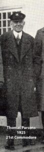Black‑and‑white portrait of a yacht club commodore wearing a suit and cap
