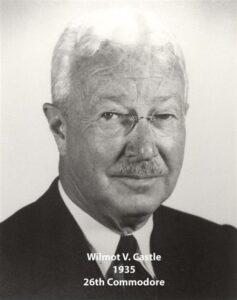 Black‑and‑white portrait of a yacht club commodore wearing a suit and cap