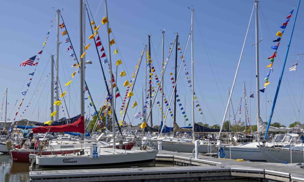 Sailboats docked in a marina with tall masts decorated with colorful signal flags and a clear blue sky overhead